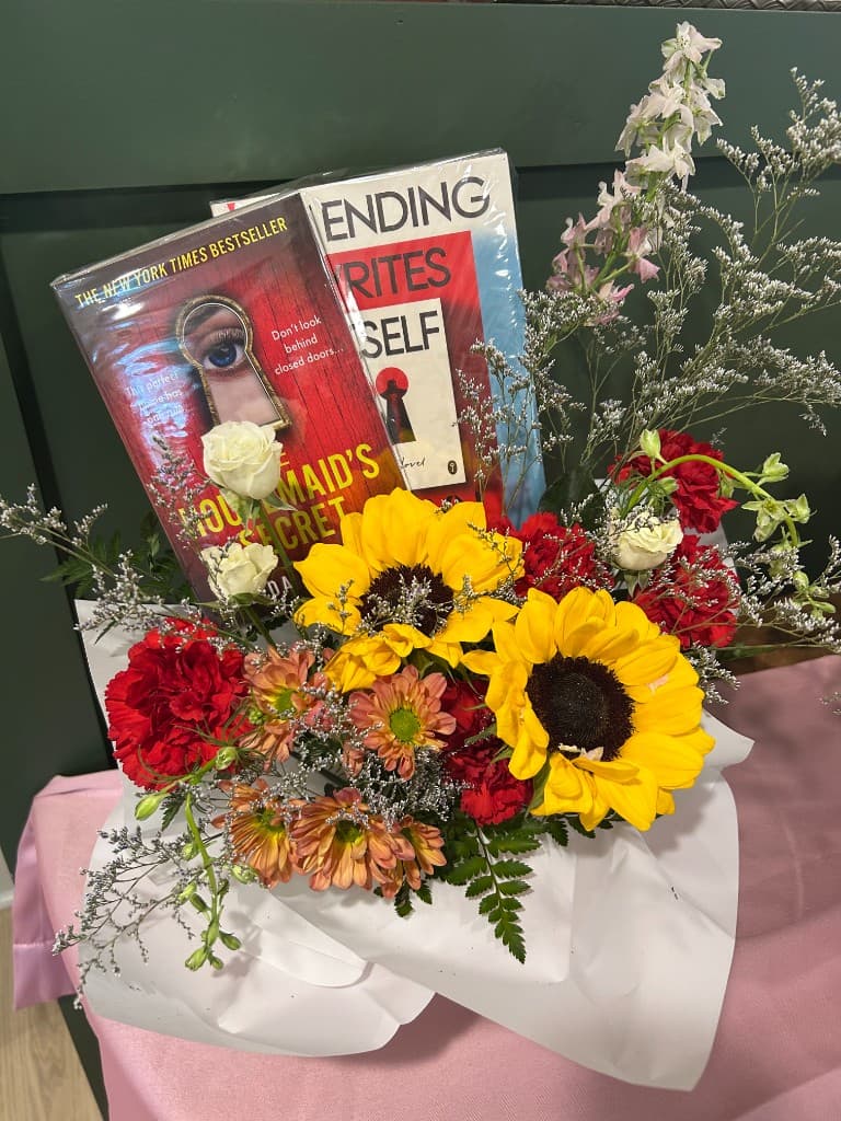 A Mother's Day Book Bouquet from Fable Books & Café featuring sunflowers, carnations, and bestselling thrillers wrapped together